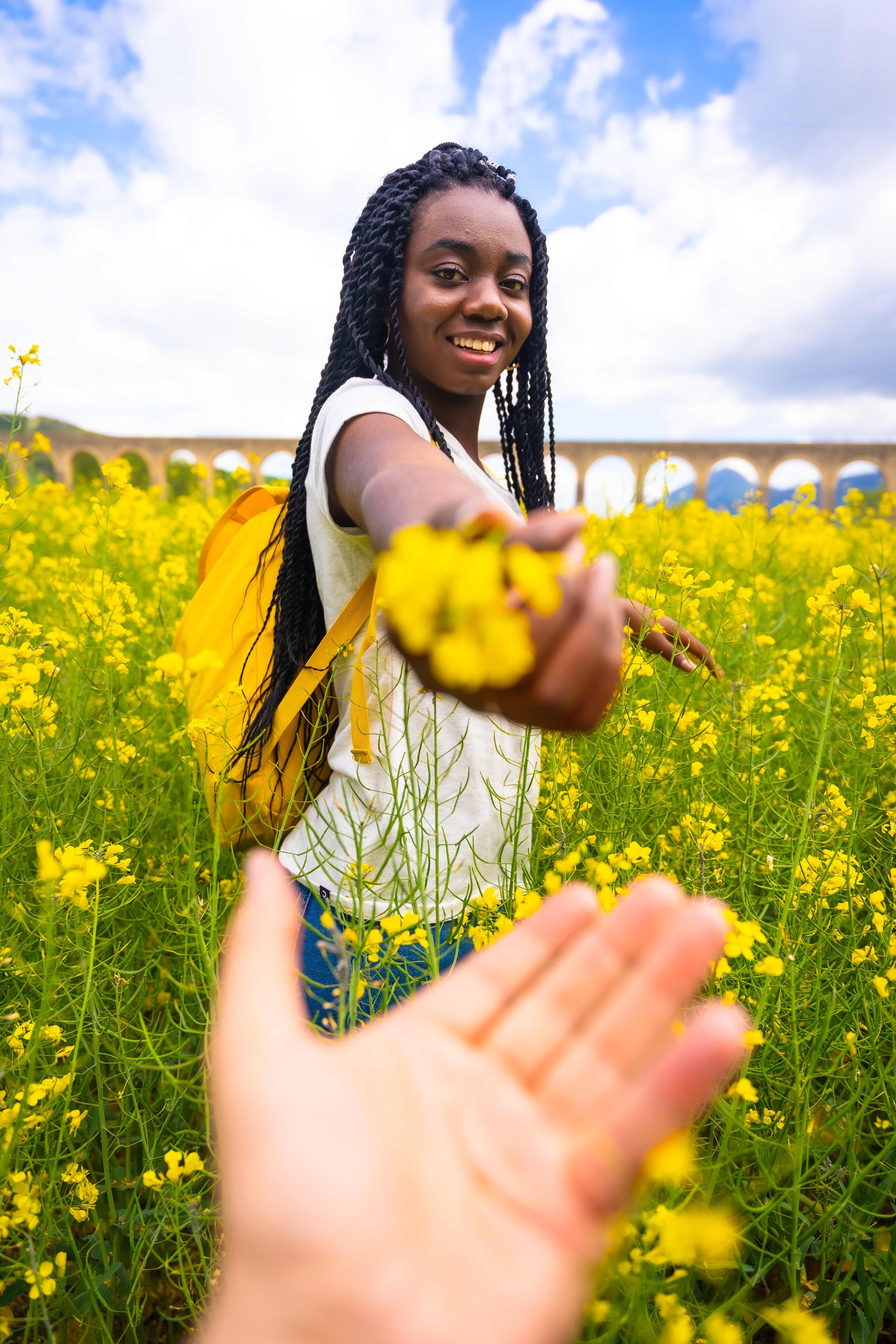 Offering a flower, a black ethnic girl with braids, a traveler, in a field of yellow flowers